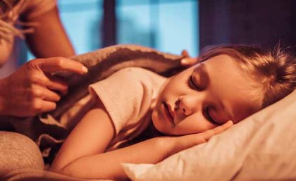 Child sleeping on her side with a mother's hands tucking the blanket around her shoulders